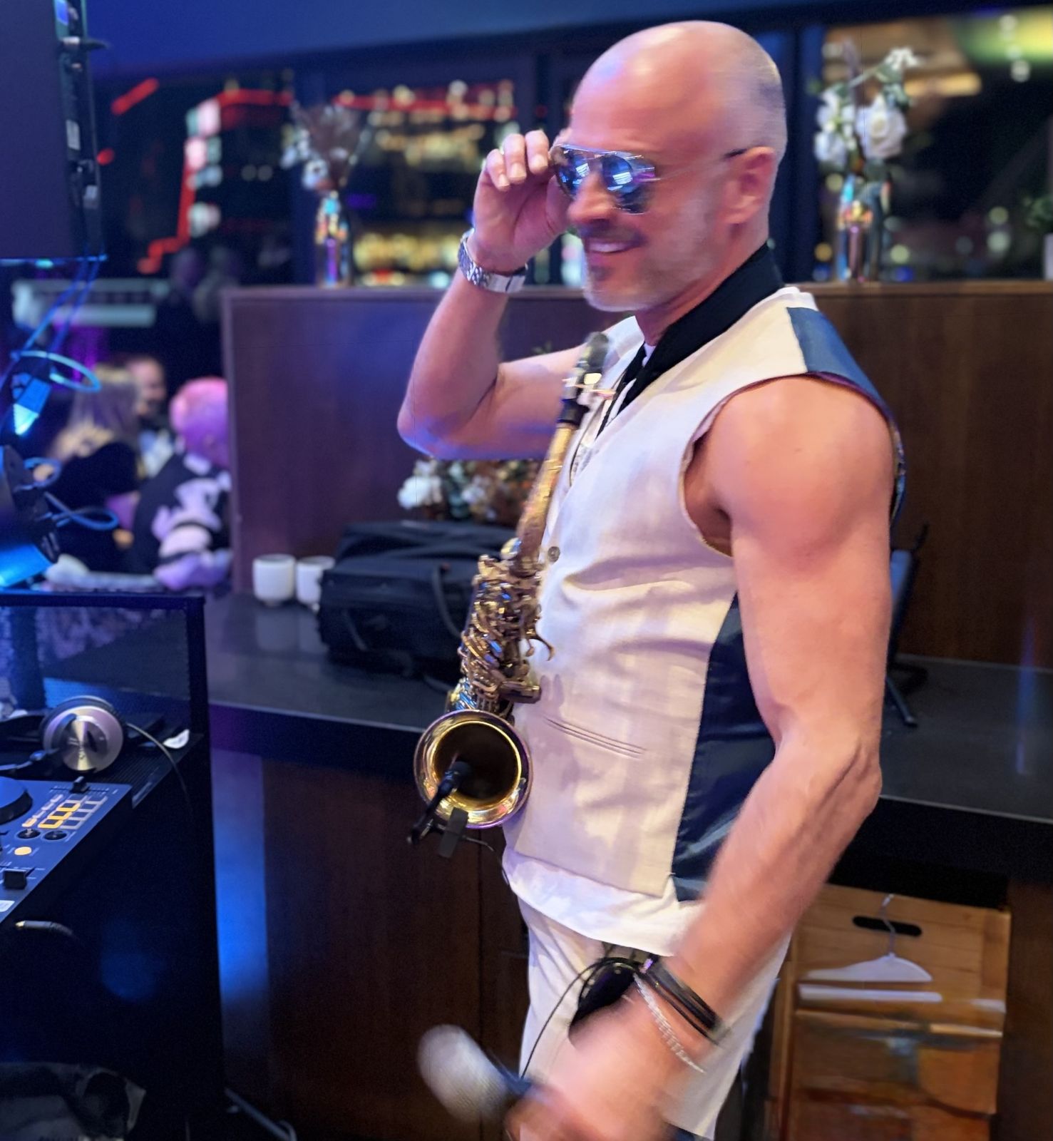 Paul Martyn with his saxophone beside a DJ controller, adjusting his sunglasses