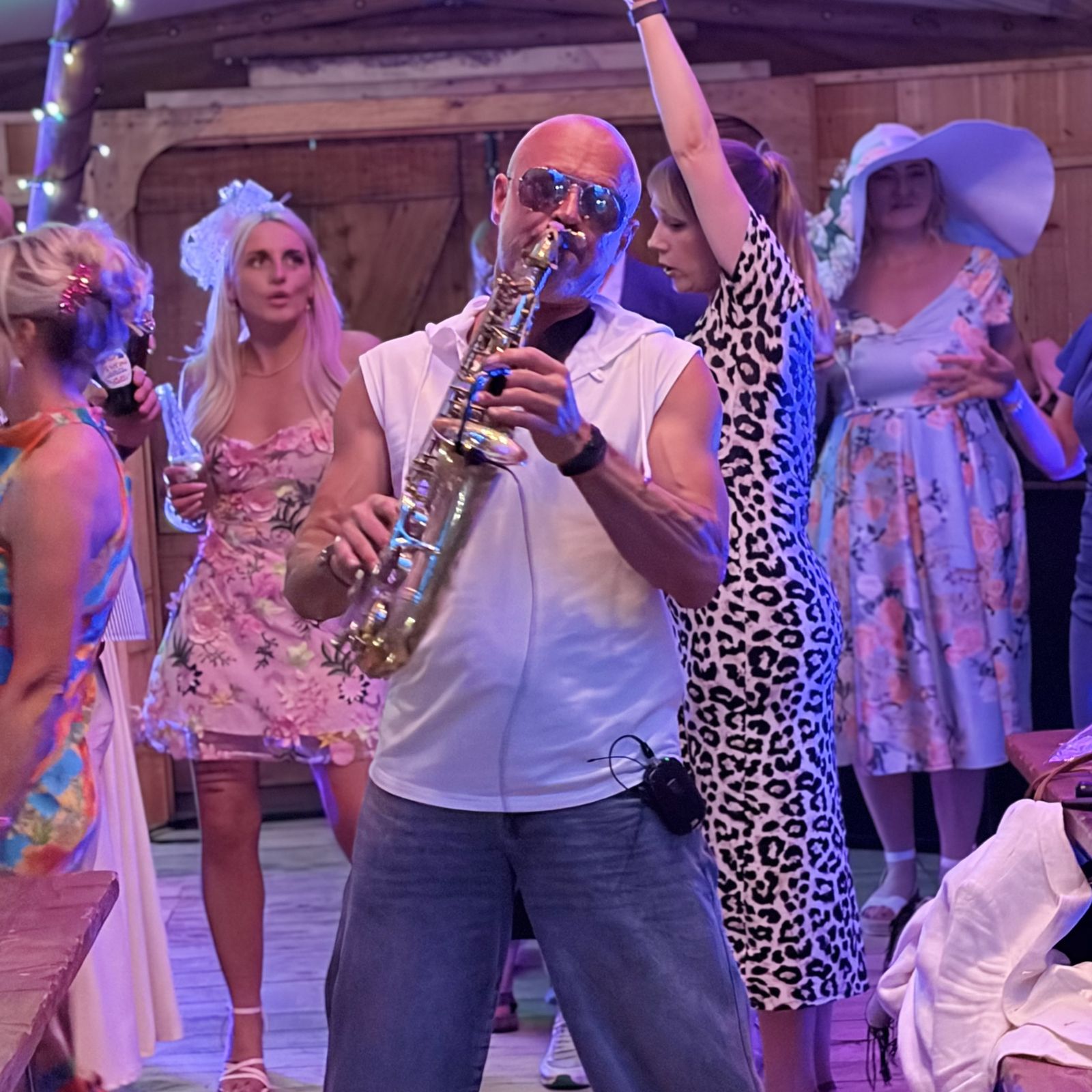 Paul Martyn playing live sax among dancing guests in summer outfits in a wooden barn venue
