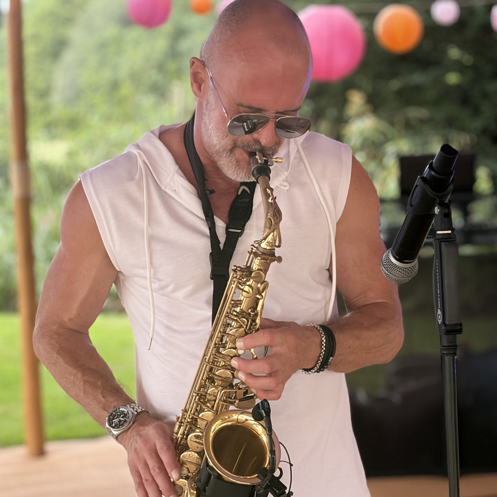 Paul Martyn playing alto saxophone at an outdoor summer party, with pink and orange paper lanterns behind him